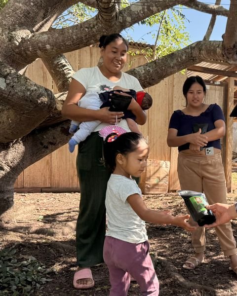 Dos productoras de APROECO, una con su bebé en brazos, mientras una niña recibe un paquete de café de la cooperativa.