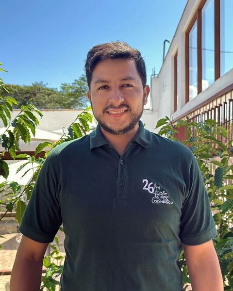 Enrique Tafur Bardales, gerente general de APROECO, sonriente con polo verde de la cooperativa entre cafetos.